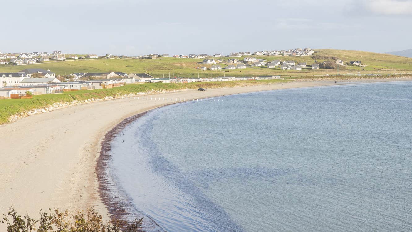 A picture of a curved beach with incoming tide and a village in the distance