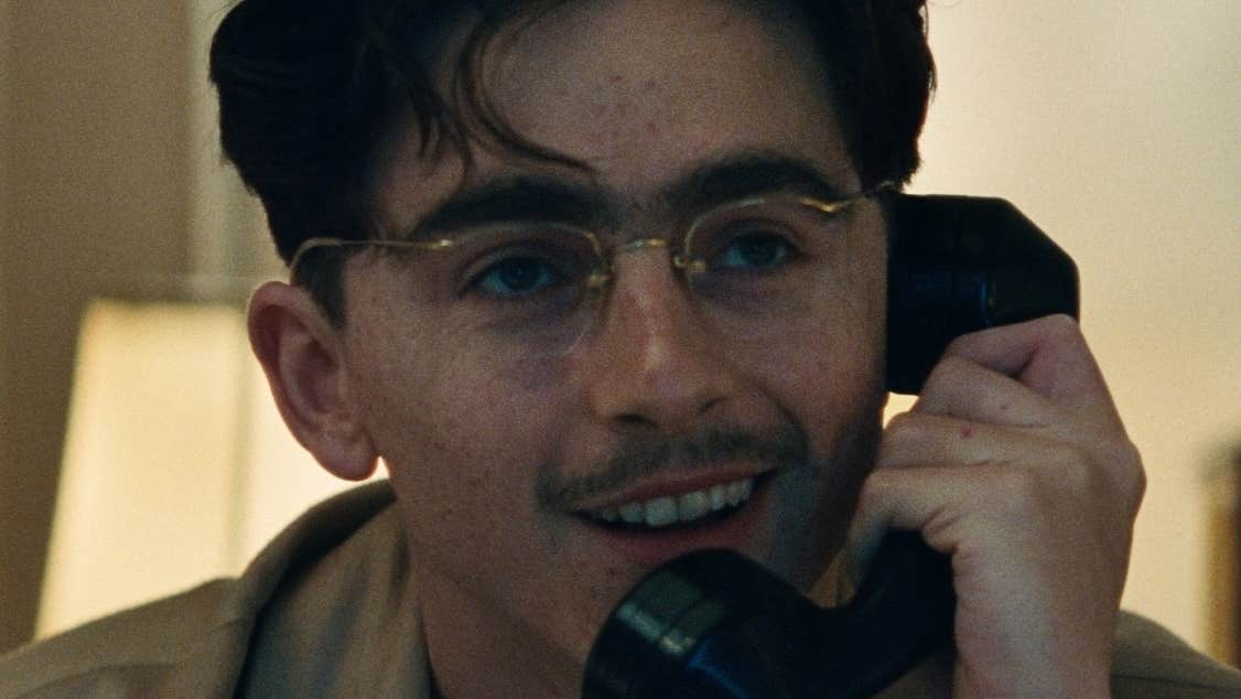 Close up view of man in glasses, smiling talking on an old style telephone.
