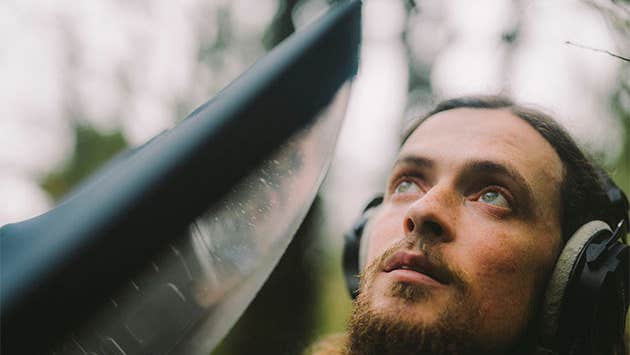 Cork ornithologist Seán Ronayne, a man outdoors wearing overear headphones looking upwards.