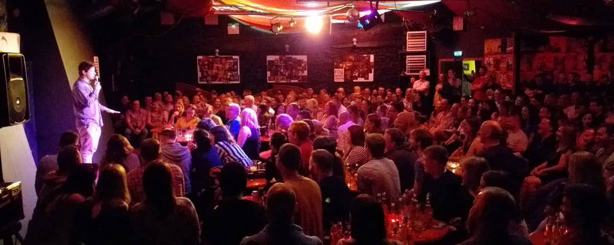 A comedian on stage during a show in front of a large audience at The Comedy Club City Limits