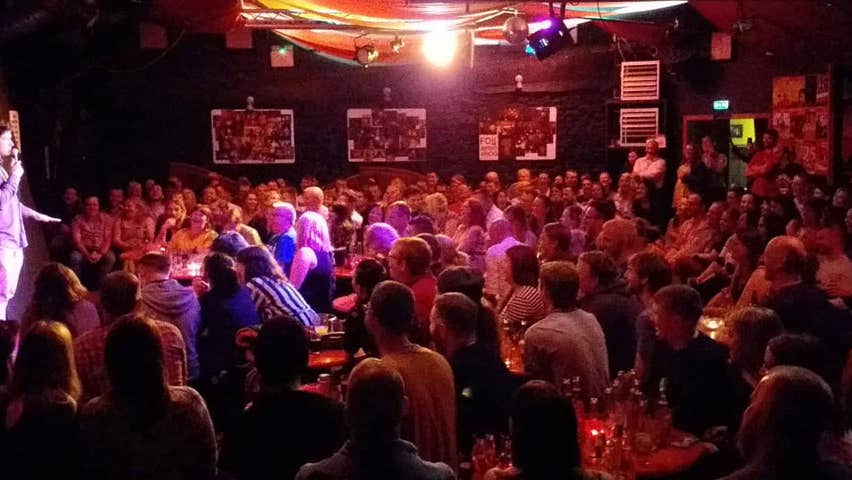 A comedian on stage during a show in front of a large audience at The Comedy Club City Limits
