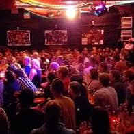 A comedian on stage during a show in front of a large audience at The Comedy Club City Limits