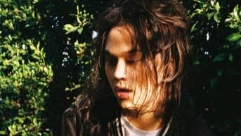 underground phenom Feng, a man with face partially obscured by hair, outside in dappled shade.