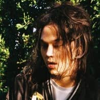 underground phenom Feng, a man with face partially obscured by hair, outside in dappled shade.