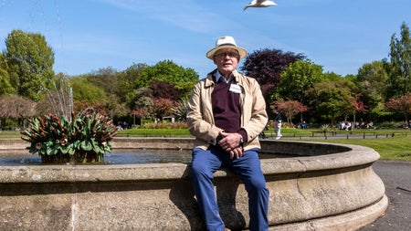 A man sitting on the wall of a fountain with a seagull flying overhead