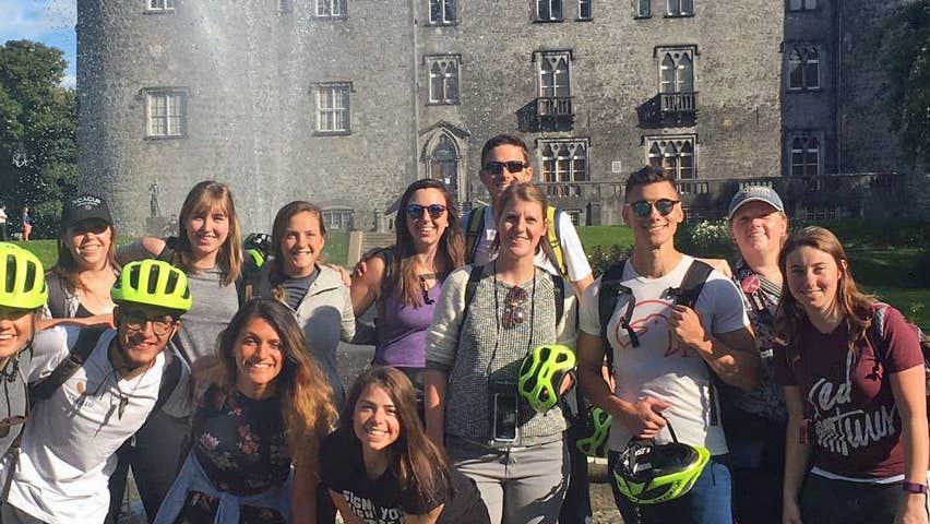 A group of cyclists on a tour with Kilkenny Castle in the background
