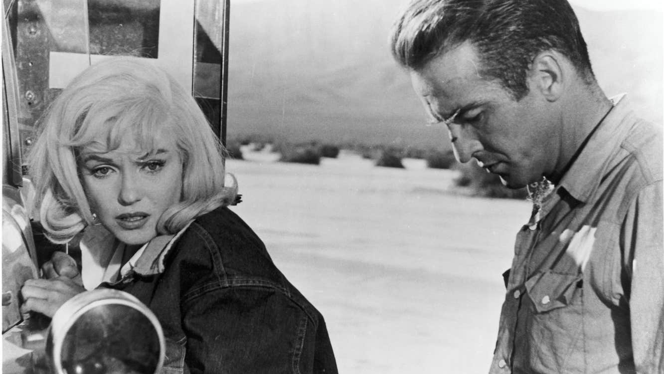 A morose man and woman next to a truck in a desert.