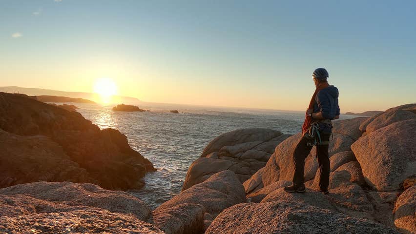 Hiker standing on a rocky coast looking at the sunset over the sea