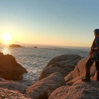 Hiker standing on a rocky coast looking at the sunset over the sea