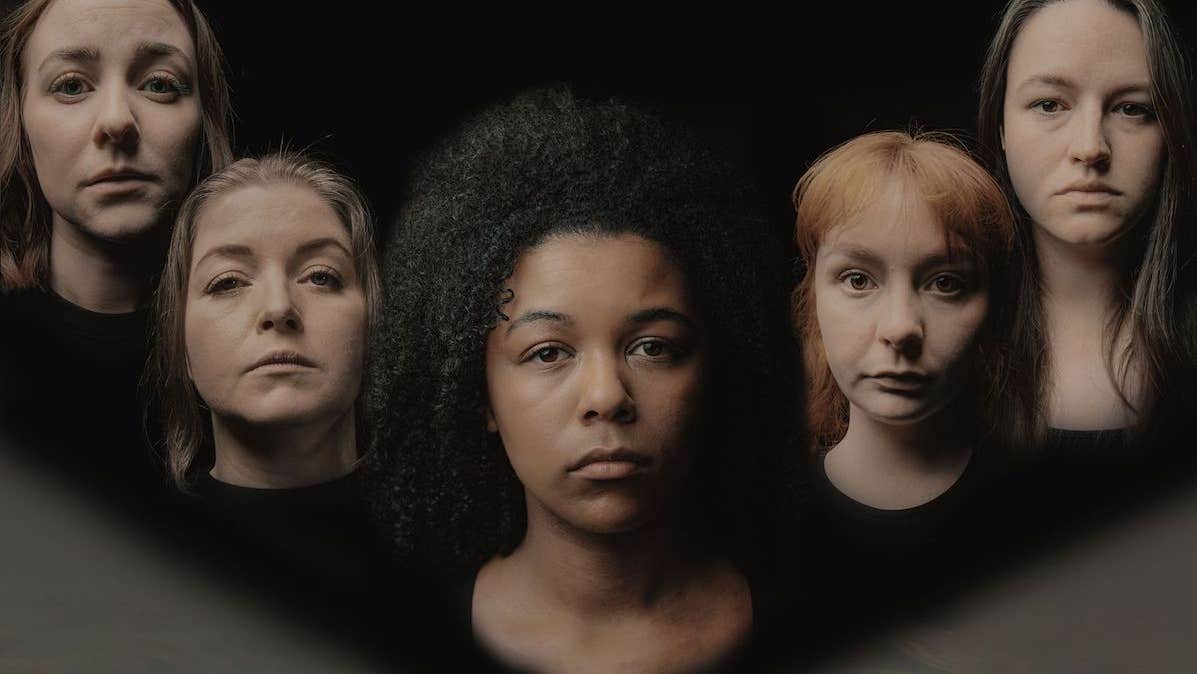 Head and shoulders of 5 serious looking women slightly blurred against dark background.