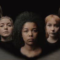 Head and shoulders of 5 serious looking women slightly blurred against dark background.