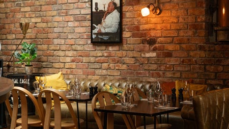A dining area with tables and chairs with the backdrop of a red bricked wall