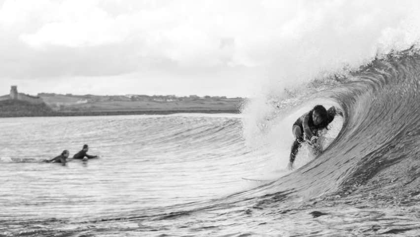 One surfer in the tunnel of a wave with two surfers paddling out to catch the wave
