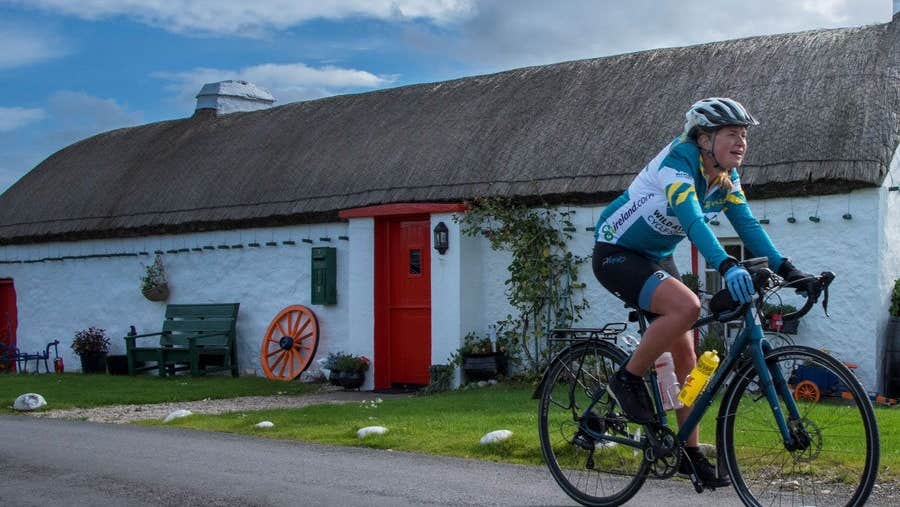 A cyclist passing a traditional thatched cottage