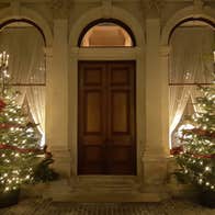 A grand, large front door with lit christmas trees either side at night.