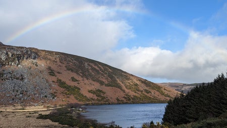 A view of a small mountain overlooking water with a rainbow over head