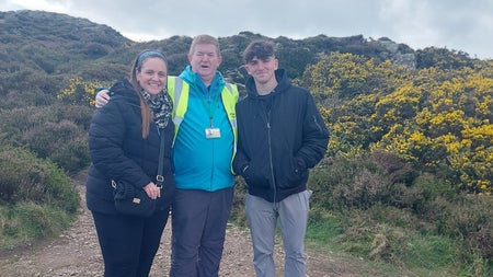 A tour guide and two clients posing for the camera surrounded by whin bushes with hills in the background