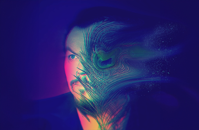 View of a face looking off to their right, lit in pink, green, blue and purple colours with a peacock's feather obscuring left hand side of the face.