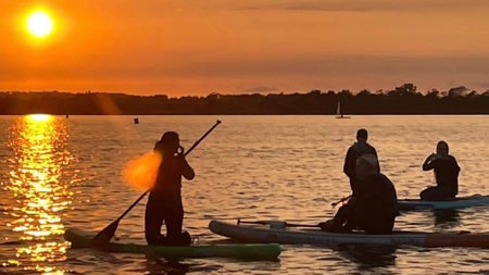 A group of people sitting on the paddle boards out on the water