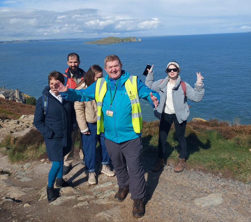 A group of people and a guide posing along a cliff top