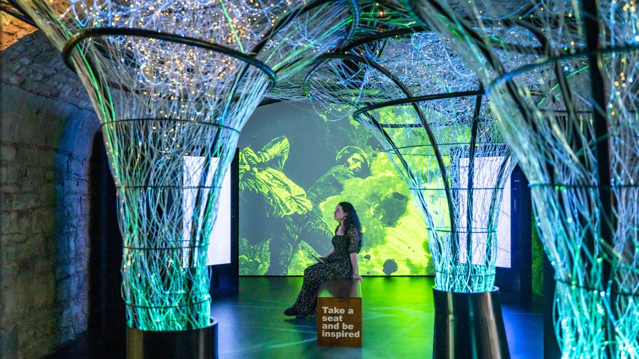 Person sitting in the middle of a room surrounded by green and blue lights