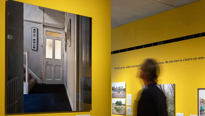 A man viewing photo art hung on a yellow wall and four other images are hanging on a wall behind him