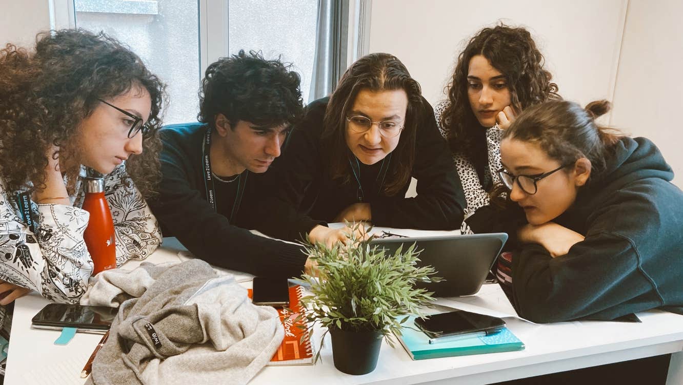 A small group of student and their tutor gather around to look at a laptop screen