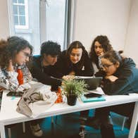 A small group of student and their tutor gather around to look at a laptop screen