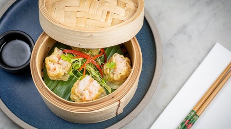 A round bamboo dish with food inside beside chopsticks