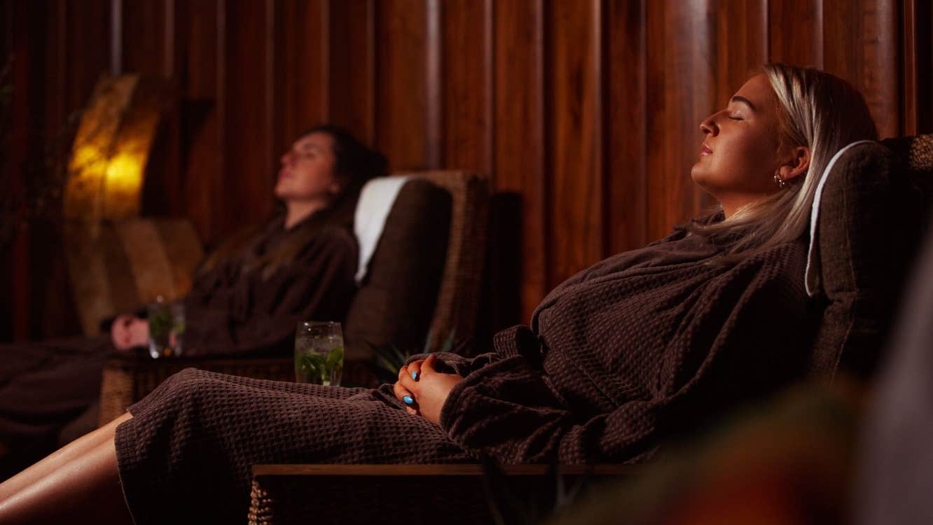Two ladies in dressing gowns relax with a healthy drink on lounge seating in a spa