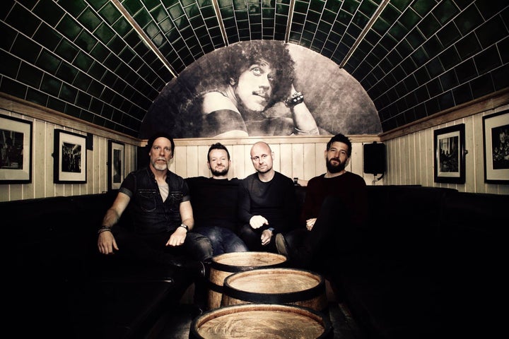 Empire Circus, a group of 4 men seated in an enclosed area with barrels in front of them.