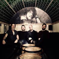 Empire Circus, a group of 4 men seated in an enclosed area with barrels in front of them.