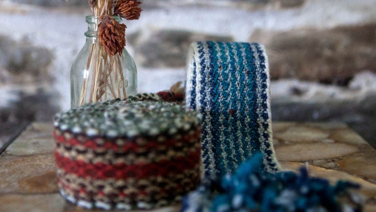 Blue and red tone crios belts displayed alongside a glass bottle