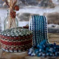 Blue and red tone crios belts displayed alongside a glass bottle
