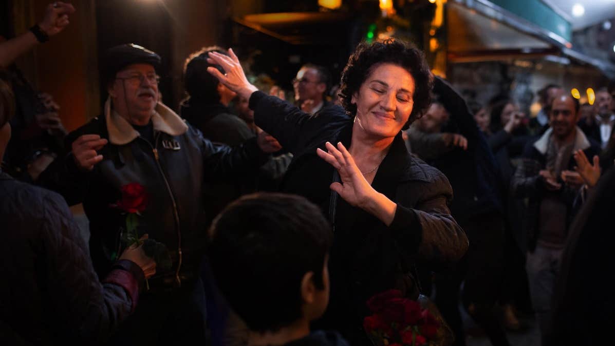 In a crowd at night a woman is dancing, smiling with her eyes closed.