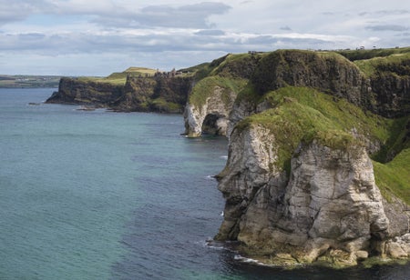 White cliffs with green grass and a faraway castle next to a blue and green coloured sea