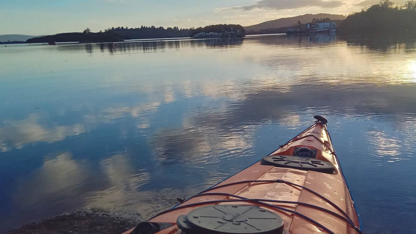 View from the front of an orange kayak overlooking the sea and bay at sunrise