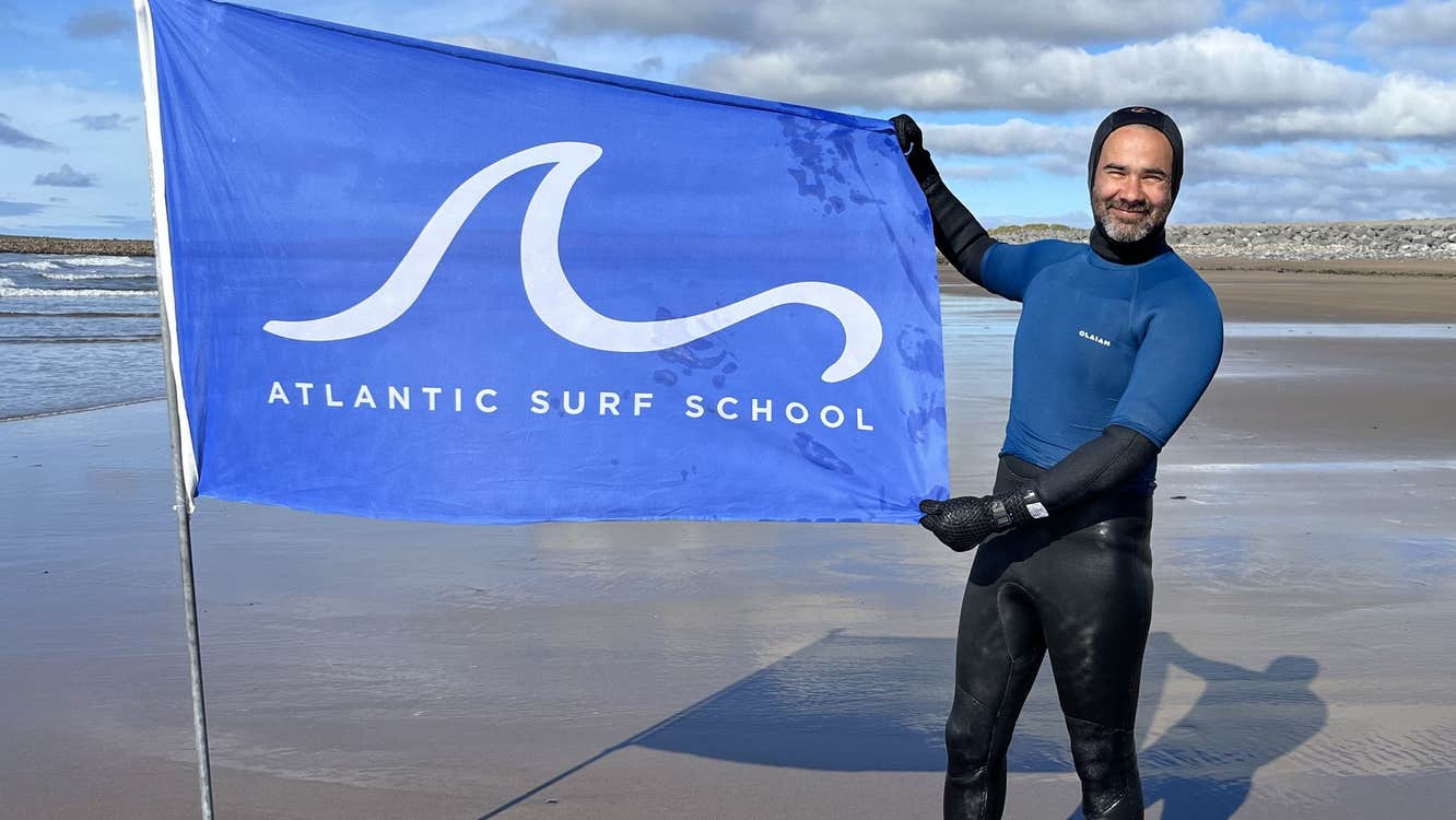 Surfer on beach in Strandhill holding Atlantic Surf School flag