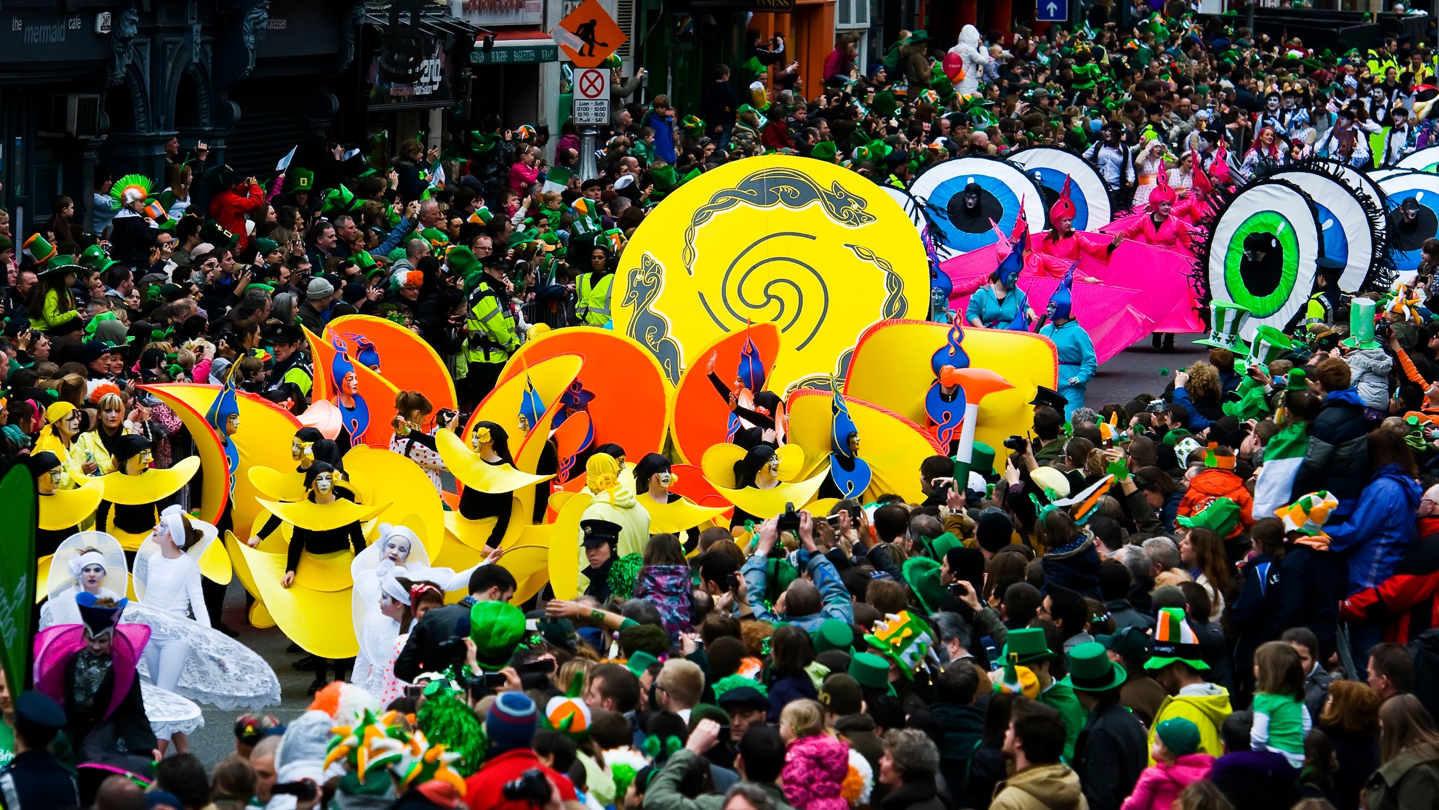 St Patricks Day parade, picturing colourful dancers with extravagant costumes and a large crowd of onlookers. 