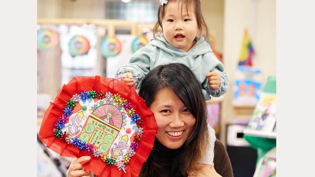 A smiling woman with a small child on her shoulders holding a craft made picture.