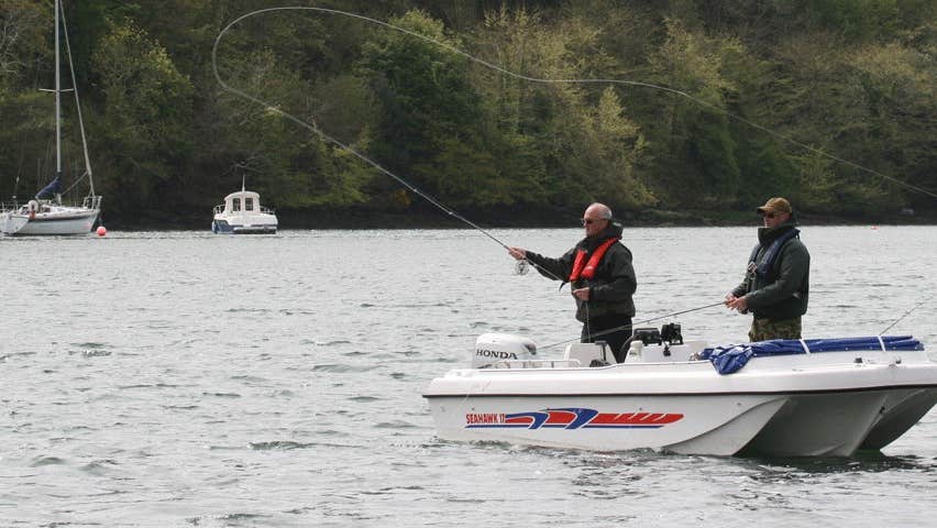 Two men with fishing rods on a boat in a harbour