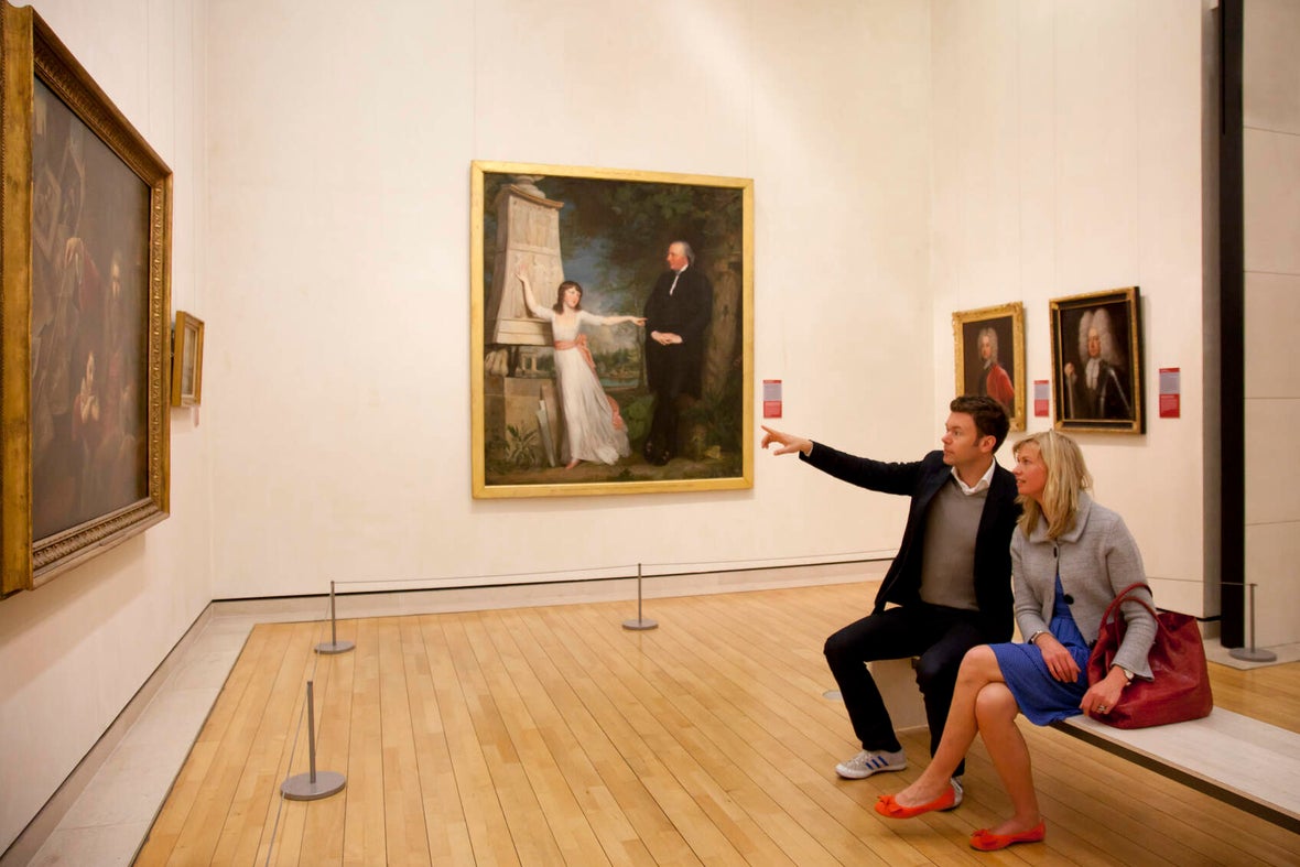 A couple sitting on a bench in the National Gallery of Ireland looking at a painting.