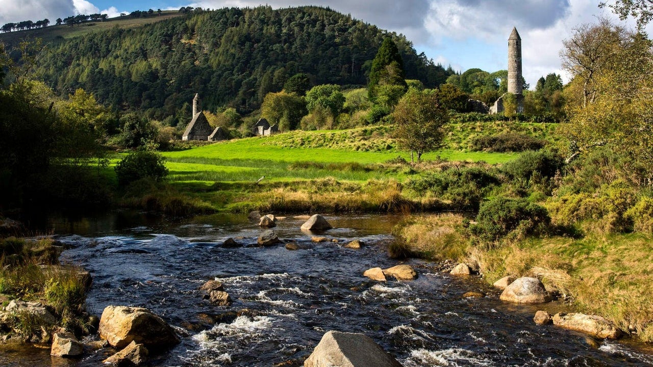 A river in front of Glendalough round tower and ancient monastic ruins