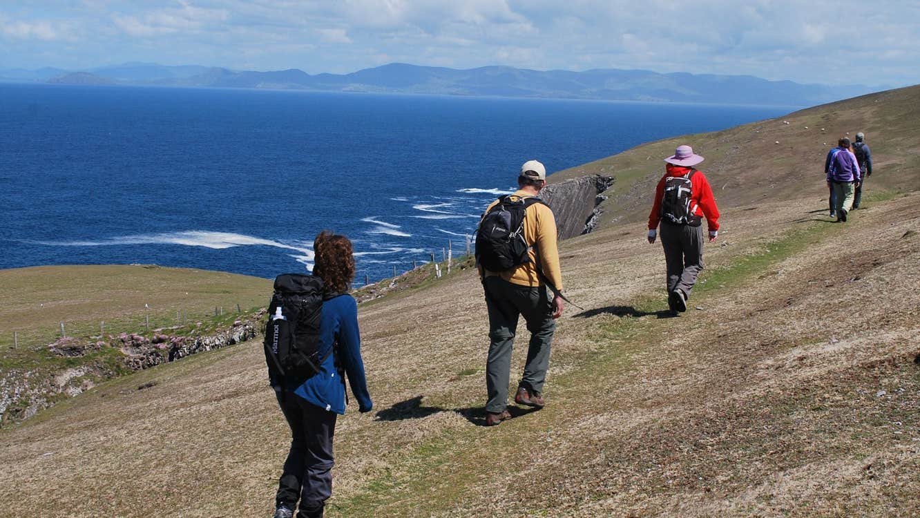 A walking group on a cliff walking with the ocean and mountains in the background