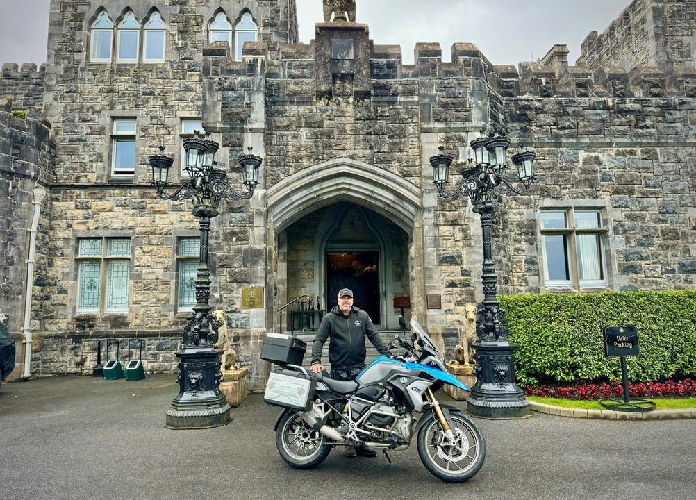 Man posing with a motorbike at a castle entrance