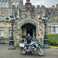 Man posing with a motorbike at a castle entrance