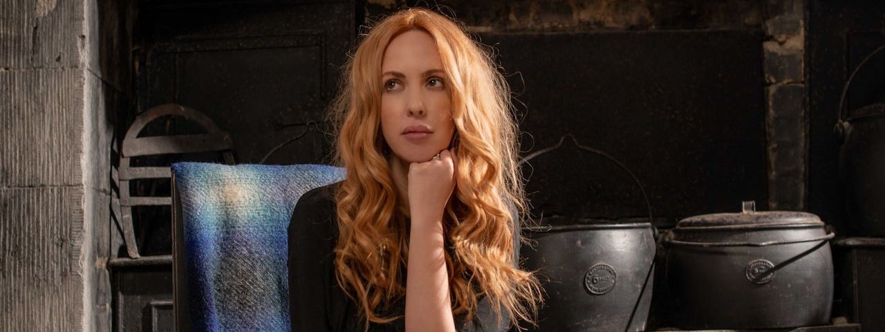 Lisa Lambe - Nightvisiting, The Hauling Home - a wistful looking woman with long wavy hair is resting her chin on raised left hand.