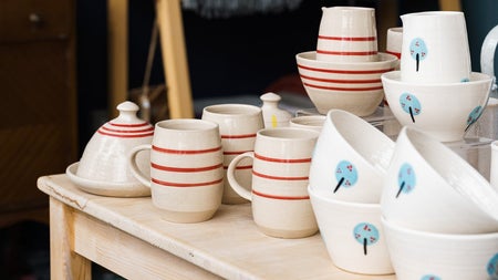 Table display of white glazed pottery with red stripes and some with a tree motif