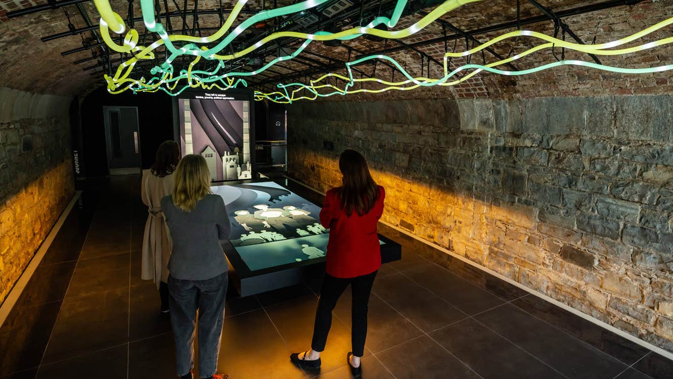 Three women looking at a large screen with coloured lights above their heads