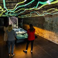 Three women looking at a large screen with coloured lights above their heads